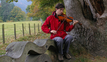 Lachlan Green sitting by Neil Gow's Fiddle Tree on the banks of the River Spey, Scotland